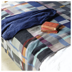 Premium Merino Lambswool throw blanket - Erno Blue, Grey & Grape block on a bed with jacket and books
