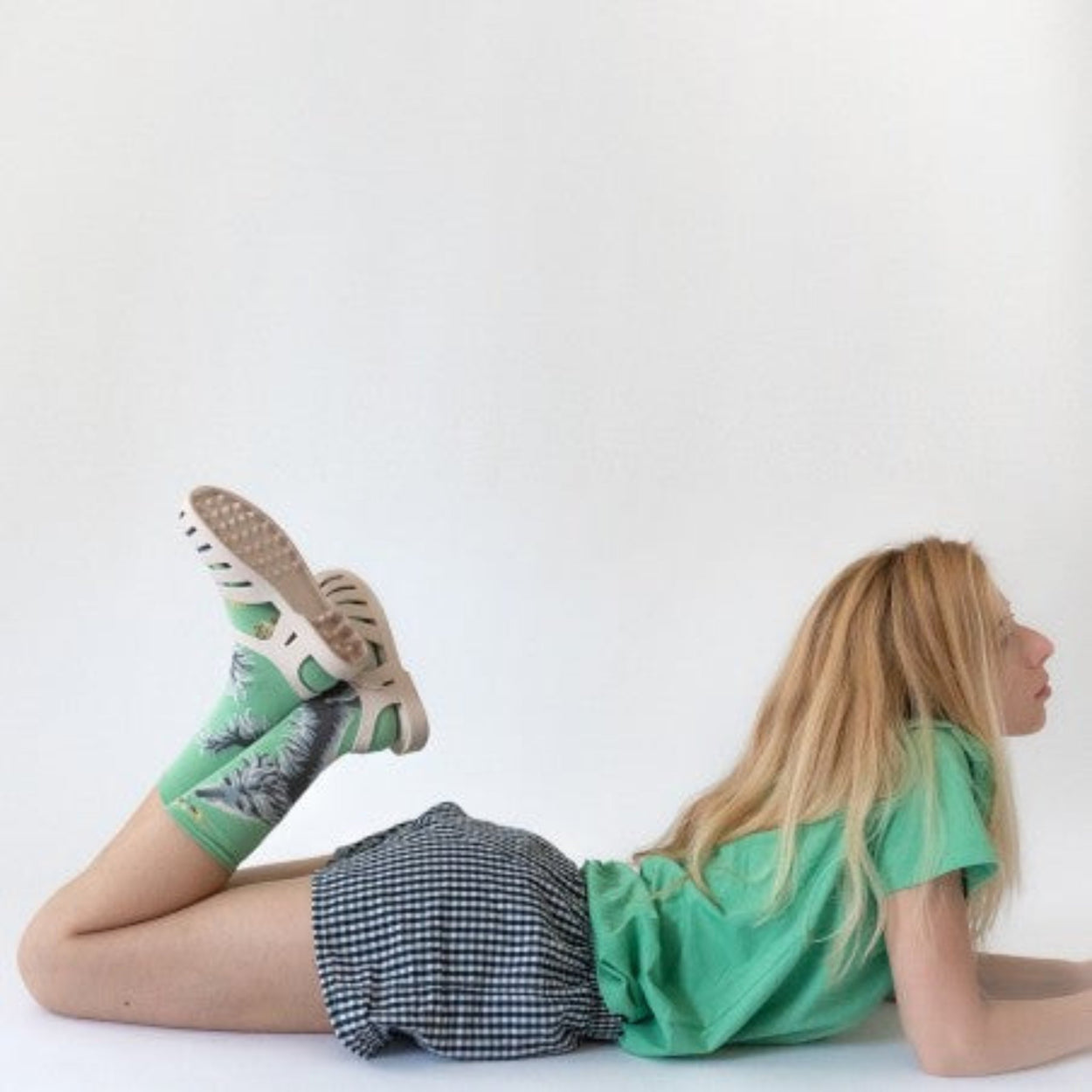 Woman in gingham shorts wearing Bonne Maison Dog Socks lying flat with knees bent.