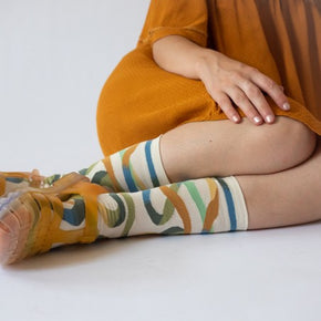 Woman in mustard dress wearing Bonne Maison Natural Ribbon Socks with orange sandals.