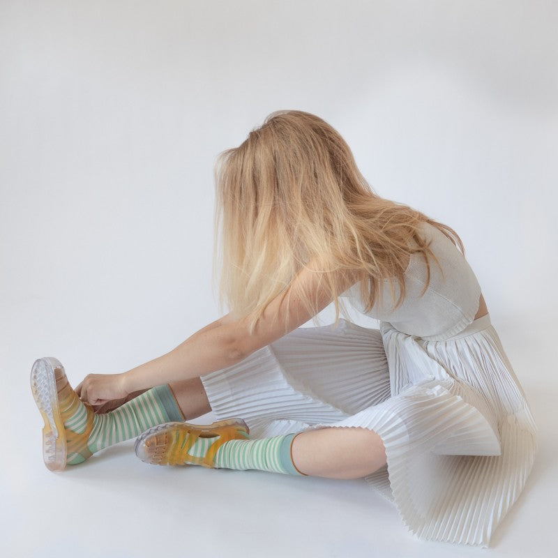 Woman sitting on ground in white clothing wearing Bonne Maison Lichen Green Stripe Socks